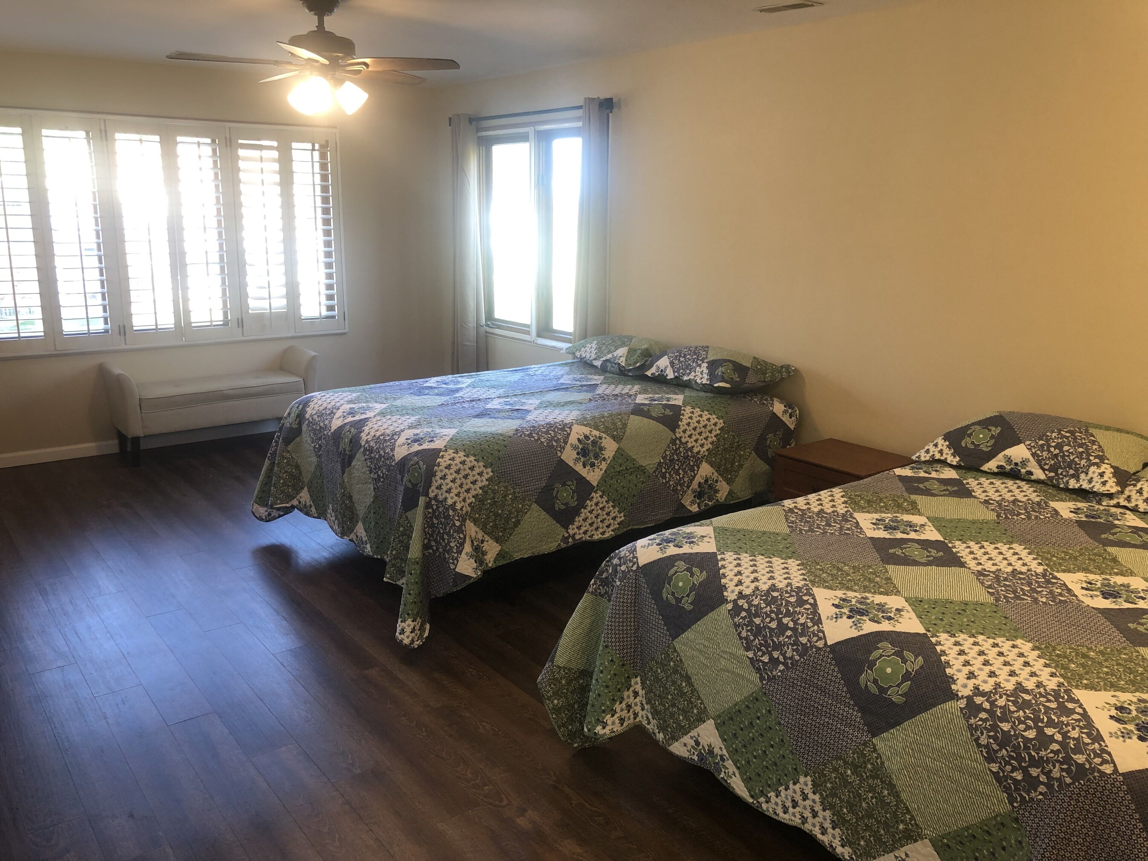 Une chambre avec deux lits, un ventilateur de plafond et une fenêtre avec des stores.
