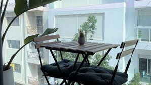 Un balcon avec une table et des chaises, un pot de fleurs et une vue sur un immeuble blanc doté de balcons.