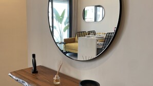 Un coin repas avec une table en bois, un miroir rond et une vue sur un canapé jaune et une table à manger, le tout visible à travers une fenêtre.