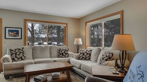 A living room with a beige sofa, patterned cushions, a wooden coffee table, and a lamp. - Chain of Lakes Waterfront Home (Central Lake)