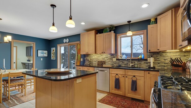 A modern kitchen with wooden cabinets, a large island, and a stone backsplash. - Chain of Lakes Waterfront Home (Central Lake)