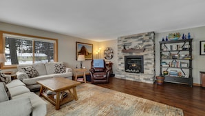 A living room with a fireplace, a sofa, a coffee table, and a bookshelf. - Chain of Lakes Waterfront Home (Central Lake)