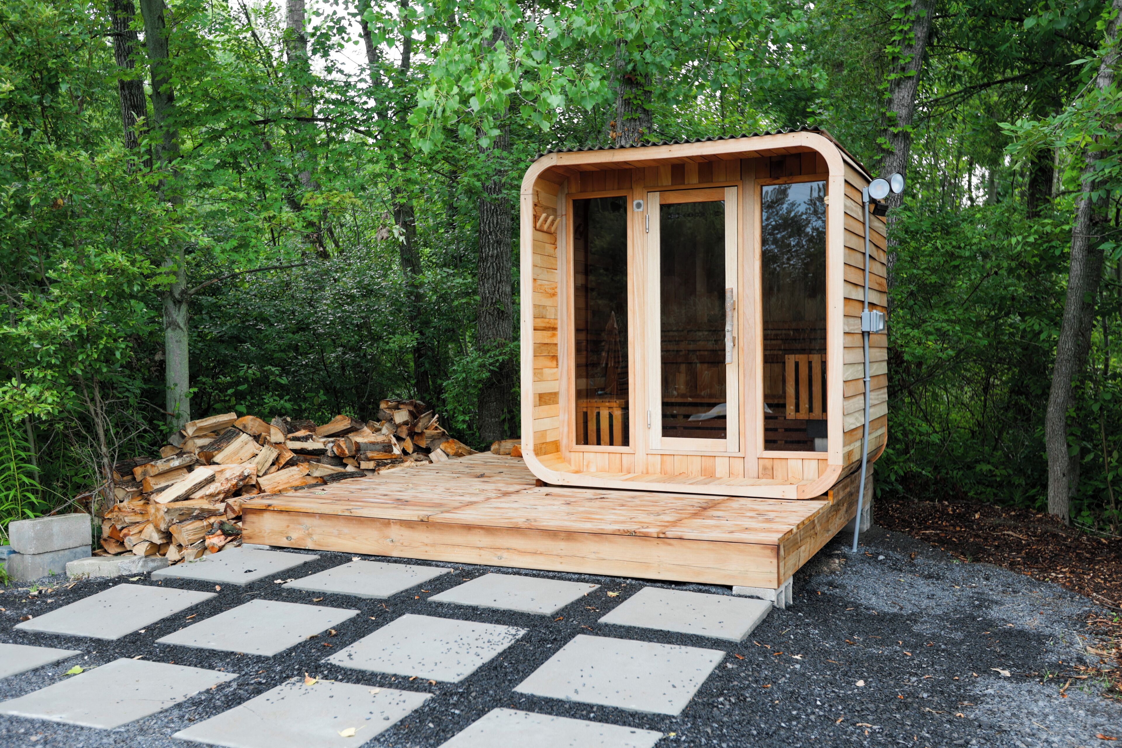 A wooden cabin with a glass door and windows, surrounded by a forest.