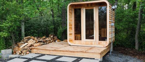 A wooden cabin with a glass door and windows, surrounded by a forest.
