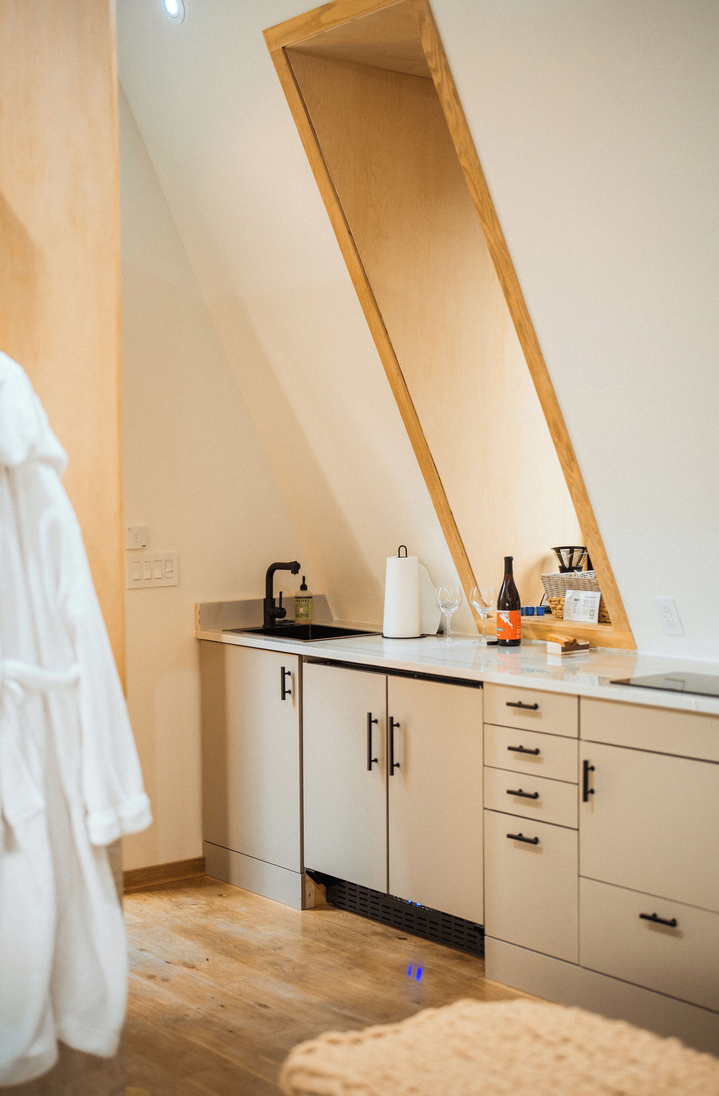 A modern bathroom with a wooden sloped ceiling, a sink with a soap dispenser, a towel rack, and a mirror.