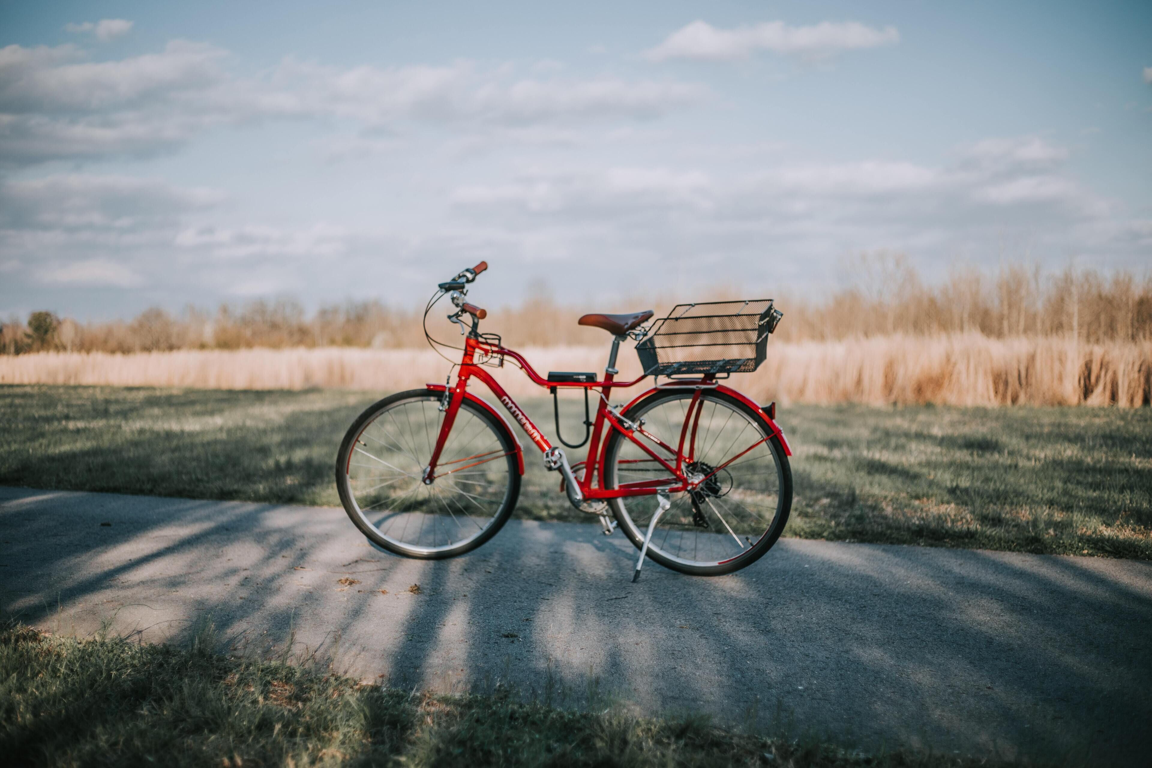 A red bicycle with a basket on a paved path in a grassy field.
