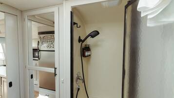 A bathroom with a shower, a towel rack, and a wall-mounted soap dispenser.