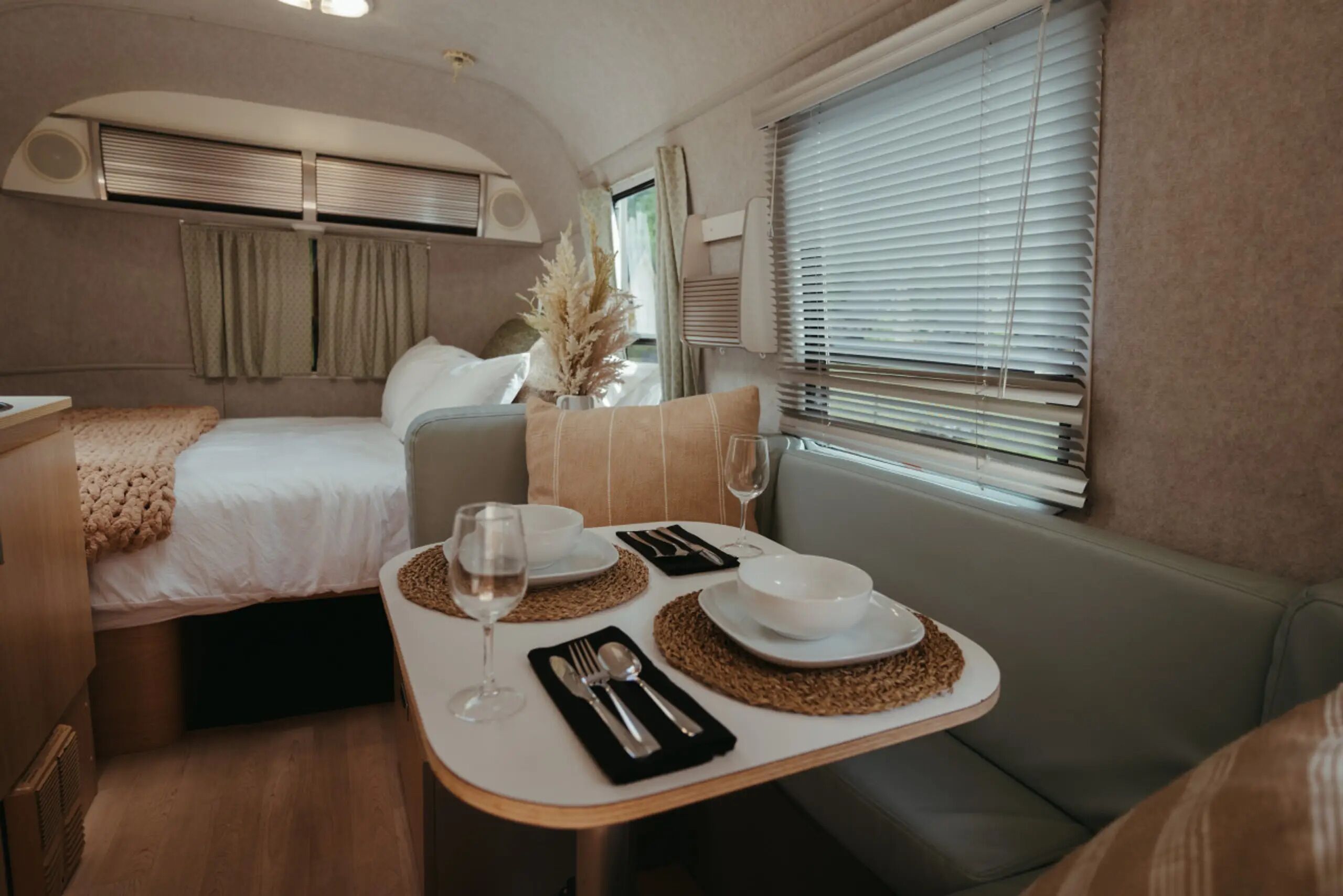 Ein gemütliches Interieur mit einem Bett, einem Essbereich mit Tisch für zwei Personen und einem Fenster mit Jalousien.