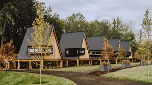 A modern building with a sloped roof, wooden exterior, and a paved pathway leading to the entrance. - Finger Lakes Treehouse & Spa (Sodus)