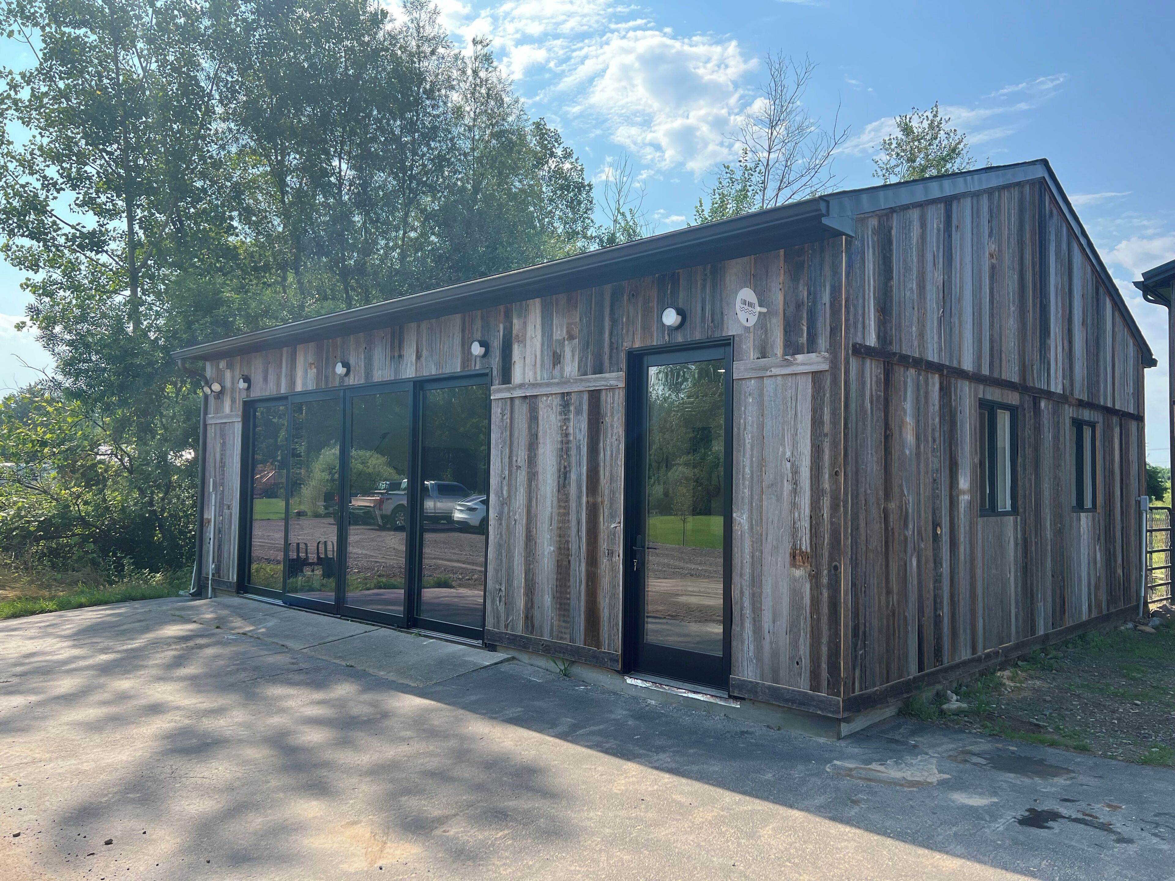 A wooden building with large glass doors and windows, a metal roof, and a paved entrance area.