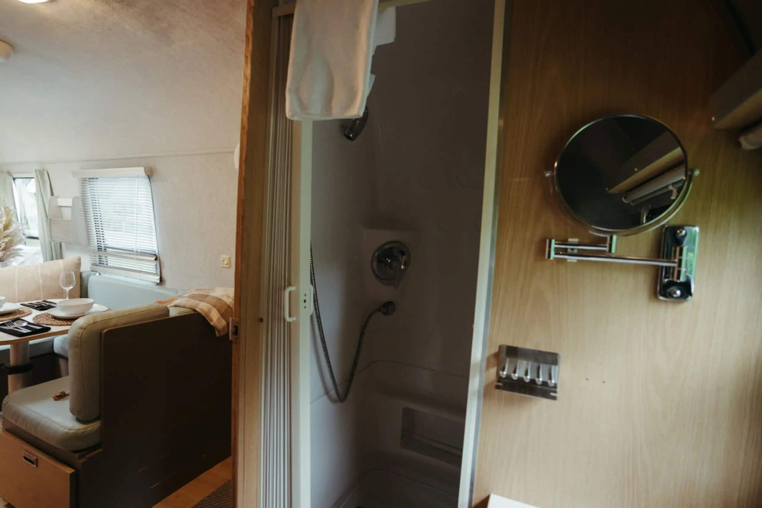 A compact RV interior with a kitchenette, a dining area, and a shower stall.