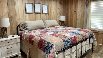 A bedroom with a wooden paneled wall, a bed with a floral quilt, two bedside lamps, a nightstand, and a window with blinds.
