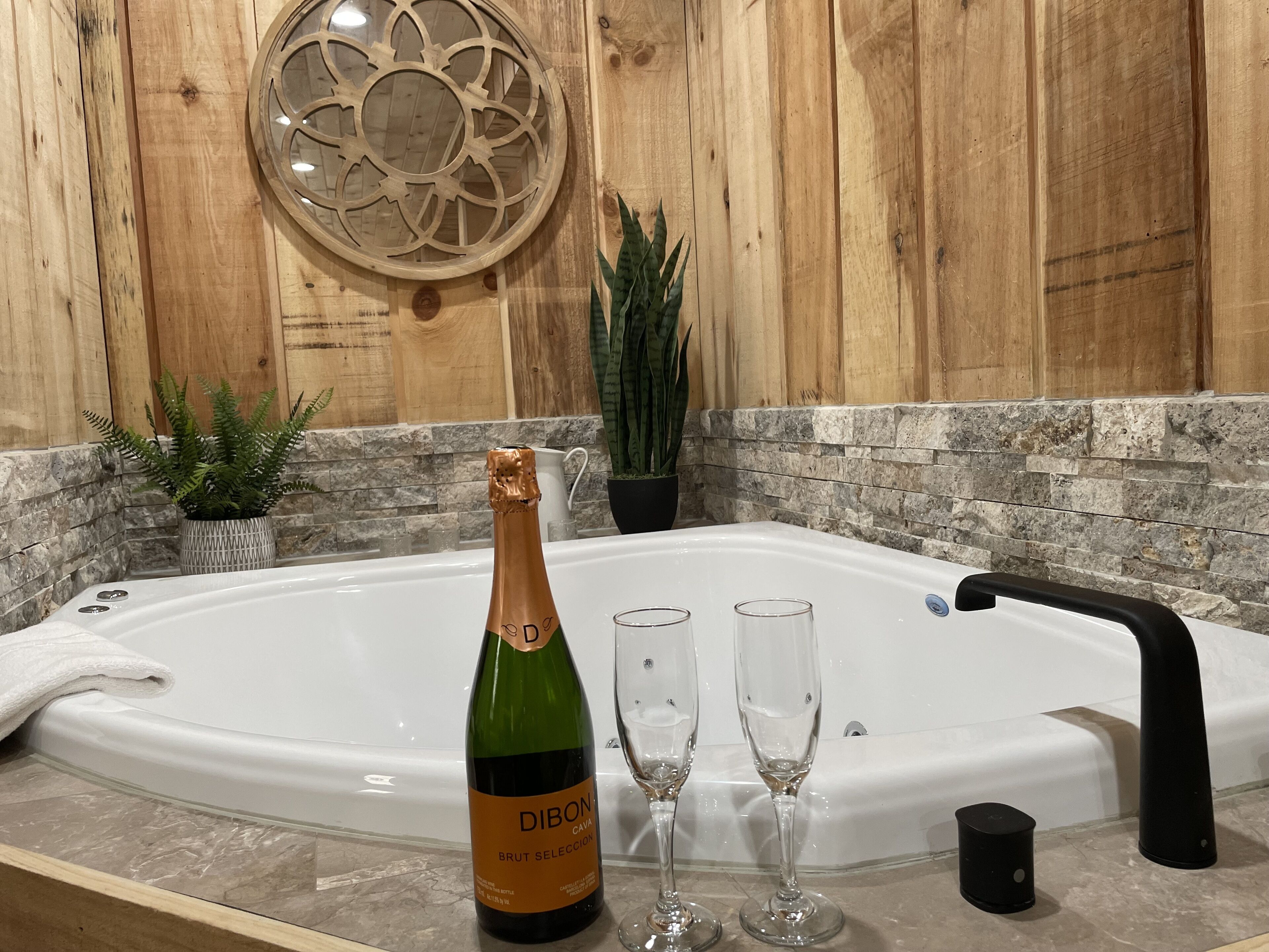 A bathroom with a large bathtub, a bottle of champagne, and two glasses.