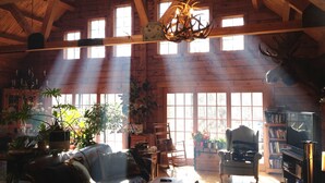 A rustic wooden interior with a high ceiling, large windows, and a chandelier.