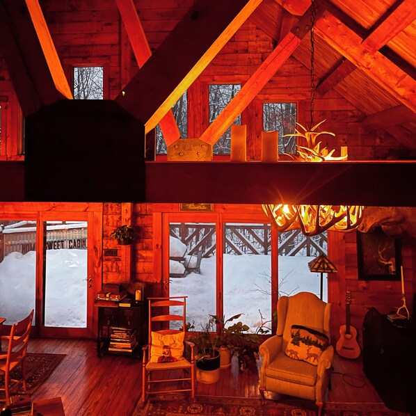 L’intérieur chaleureux d’un chalet, avec un décor en bois, une cheminée, un fauteuil et une guitare.