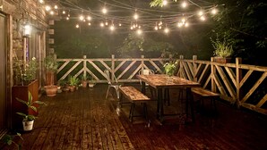 An outdoor patio with wooden tables and chairs, string lights, and potted plants.