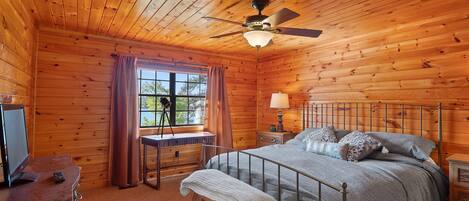 Ein Schlafzimmer einer Holzhütte mit einem Bett, einem Schreibtisch, einem Stuhl, einer Lampe und einem Deckenventilator.