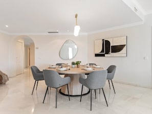 A modern dining area with a round table, grey chairs, a large mirror, and abstract art on the wall.