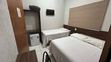 Quarto pequeno e limpo, com duas camas de solteiro, uma escrivaninha, um frigorífico e uma televisão na parede.