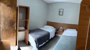 A compact hotel room with a wooden wardrobe, two beds, a small bedside table, and a wall-mounted picture.