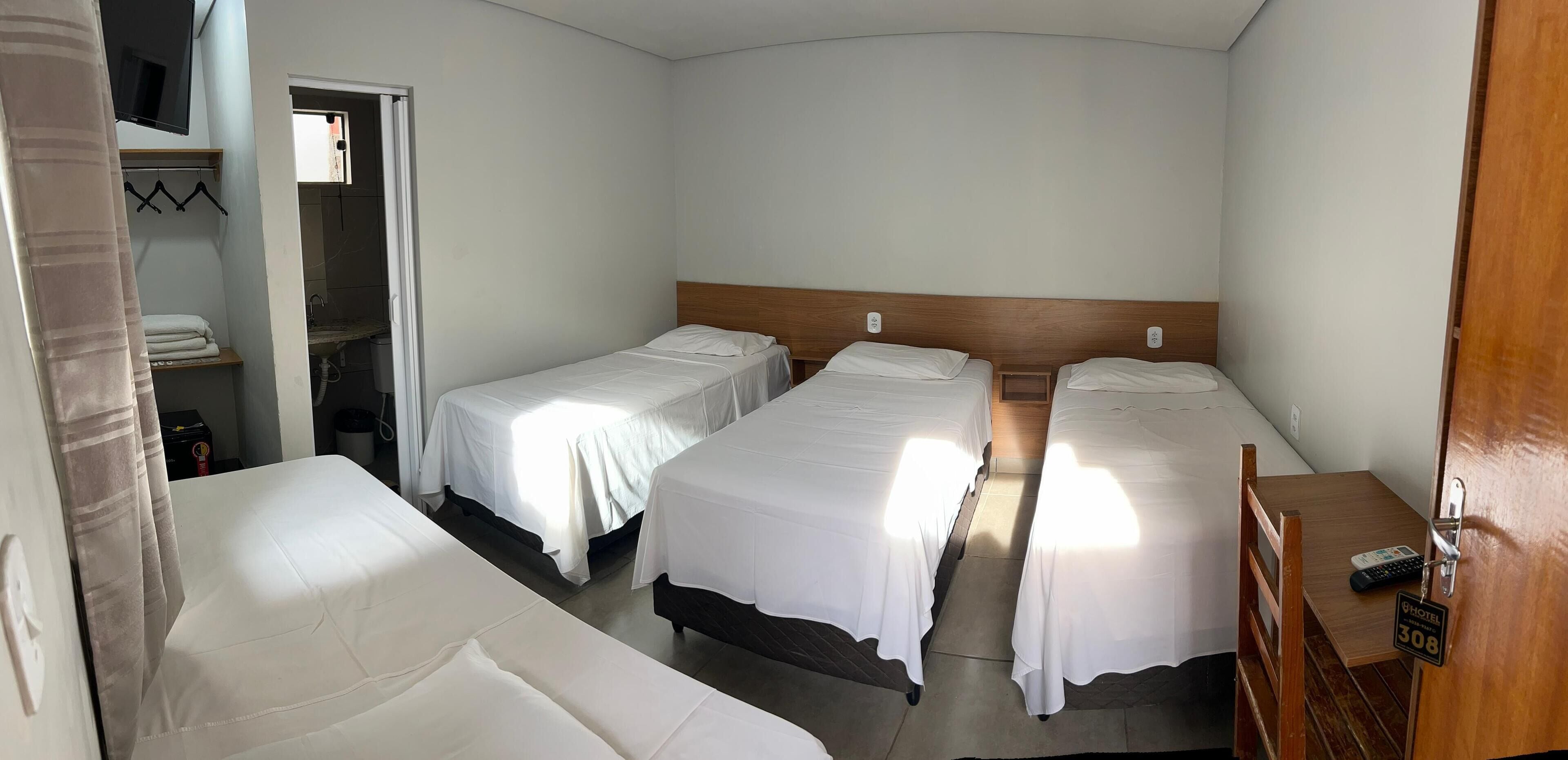 A hotel room with three single beds, a wooden headboard, a small table, and a TV mounted on the wall.