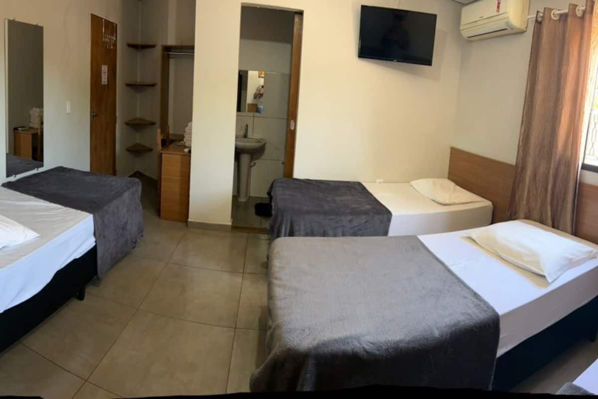 Hotelkamer met vier enkele bedden, een zithoekje, een televisie en een zichtbare badkamer door een geopende deur.