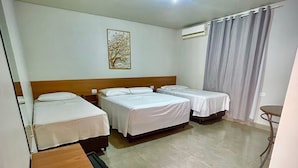 Habitación de hotel con tres camas, un escritorio de madera, una mesita pequeña y una lámpara en el techo.