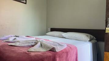 A single bed with a white mattress and two white pillows, a pink blanket, and a white towel.