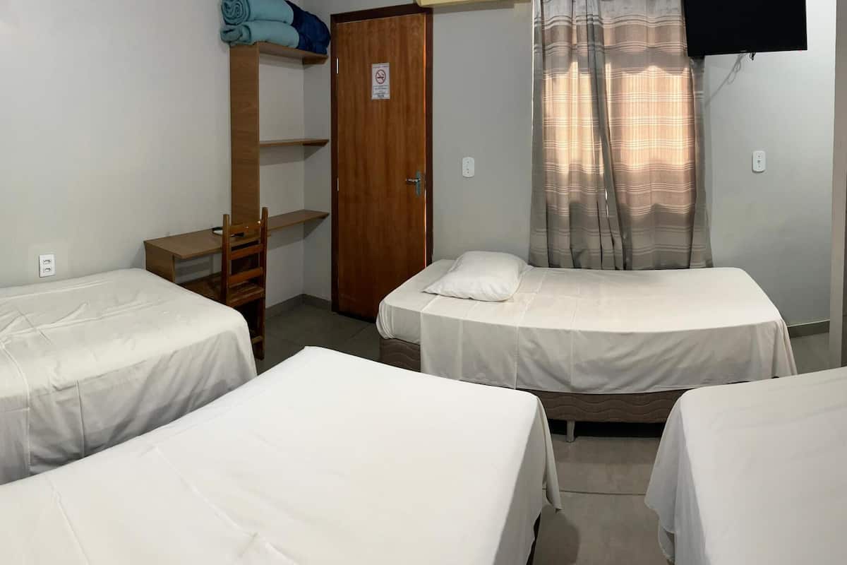 Een kleine, schone kamer met twee enkele bedden, een houten garderobe, een bureau en een aan de muur bevestigde televisie.