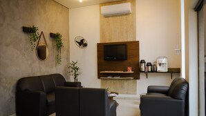 Una sala de estar moderna con dos sofás de cuero negro, un televisor montado, una cafetera y una mesita con una planta.