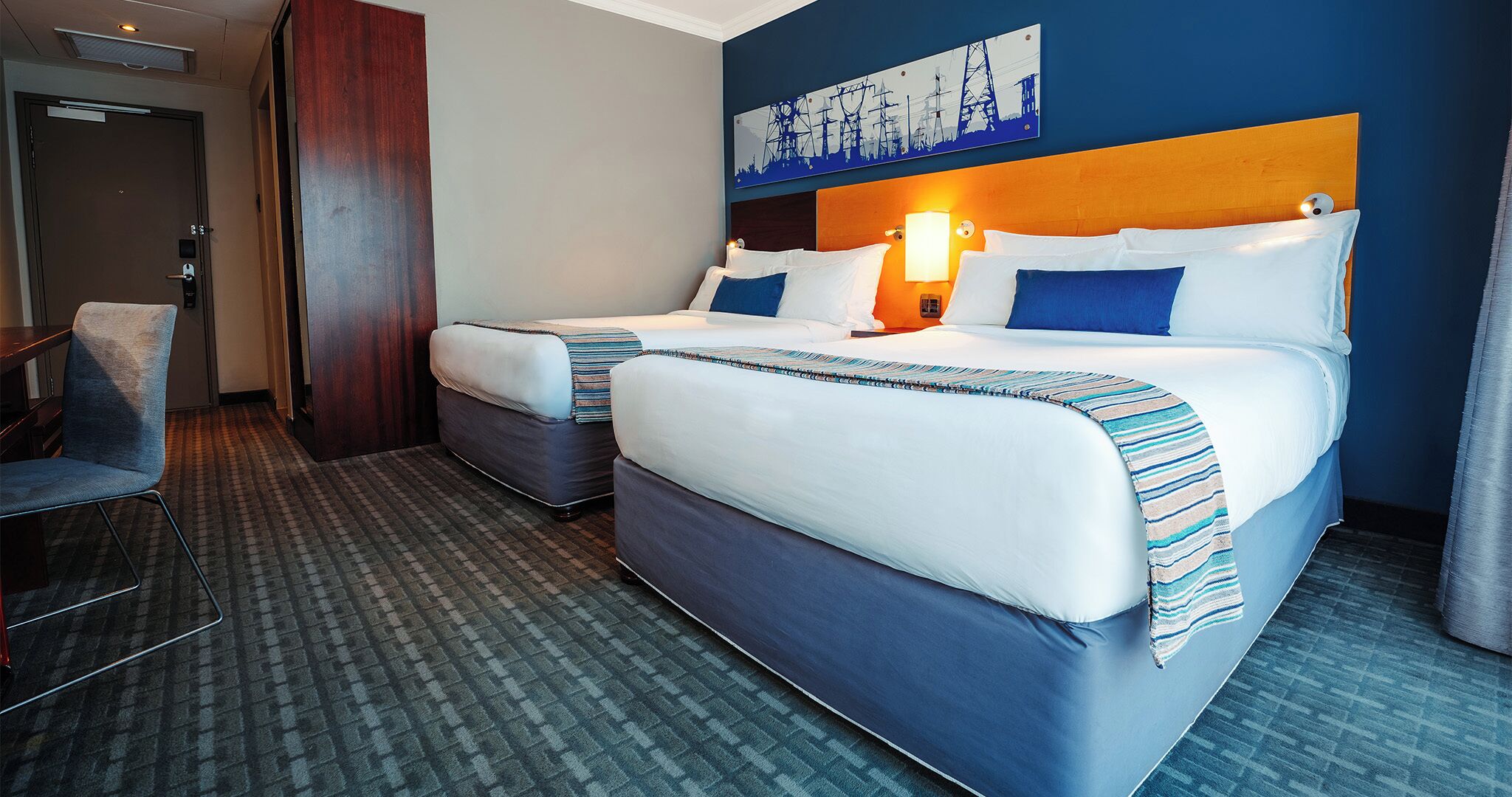 A hotel room with two beds, a desk, and a chair.