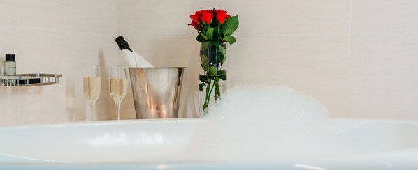 A bathtub with bubbles, a champagne bottle, a glass of champagne, and a red rose. - Blackrock Hotel (Newcastle)