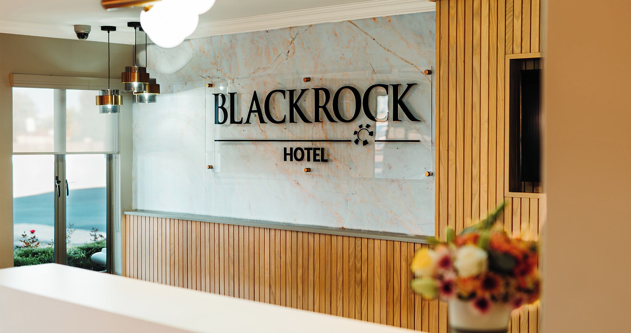Un área de recepción con pared de mármol, diseño de paneles de madera y un cartel que dice "BLACKROCK HOTEL".