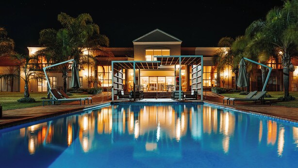 A swimming pool with lounge chairs and a covered seating area in front of a building at night. - Blackrock Hotel (Newcastle)