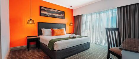 Een hotelkamer met een groot bed, oranje wanden, een stadsgezicht foto, een bureau en een stoel.