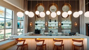 A modern bar area with a central island, bar stools, and a large window providing a view of the outdoors. - Blackrock Hotel (Newcastle)