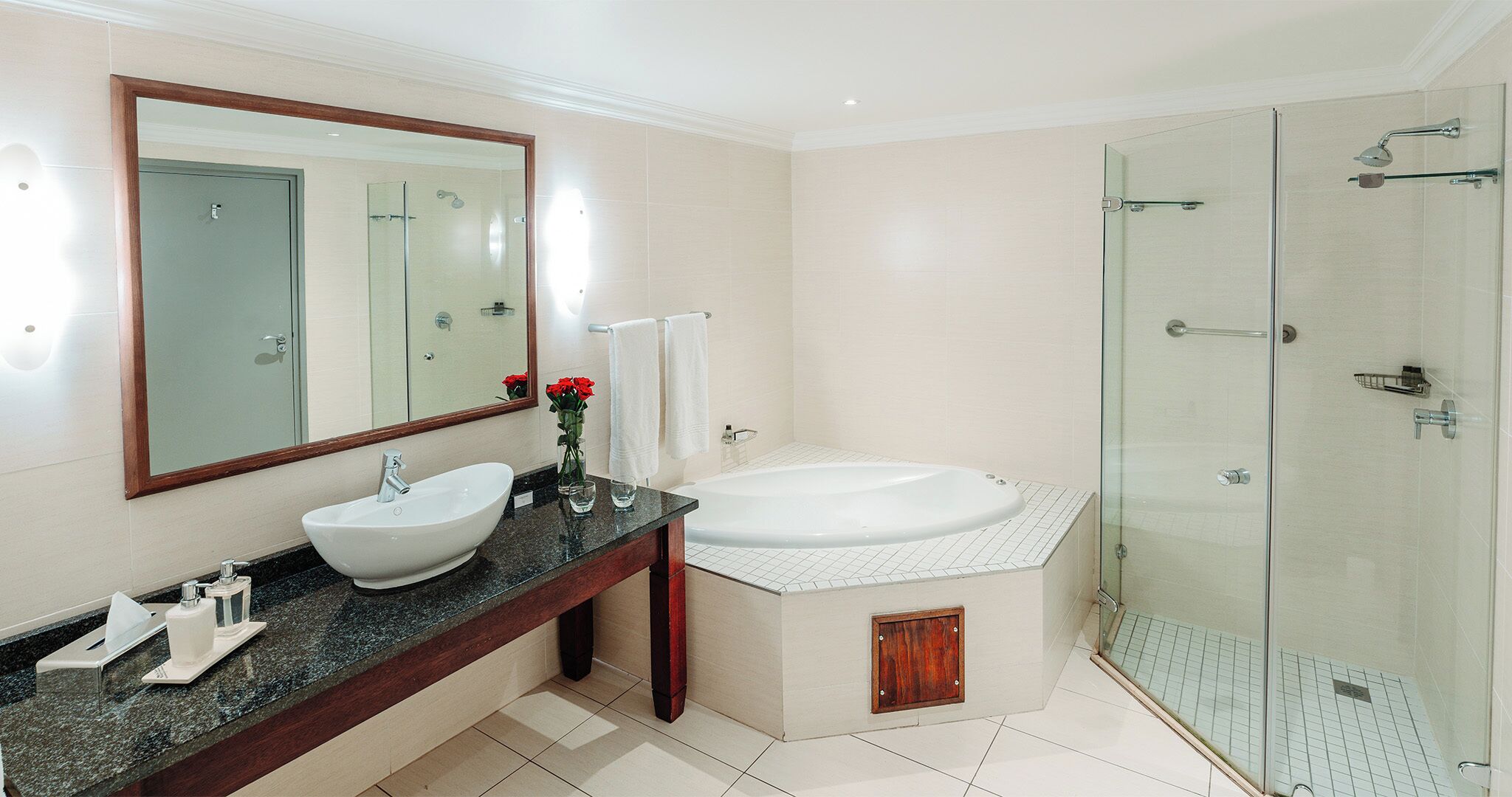 Une salle de bain moderne avec un double vasque, un grand miroir, une douche à parois de verre et un meuble-lavabo en bois.