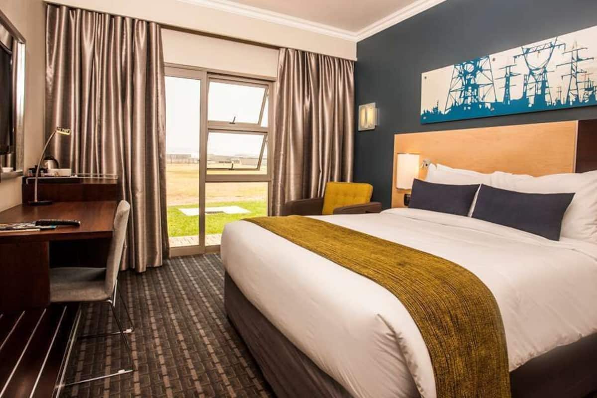 Quarto de hotel com cama, escrivaninha, cadeira e vista para o exterior.