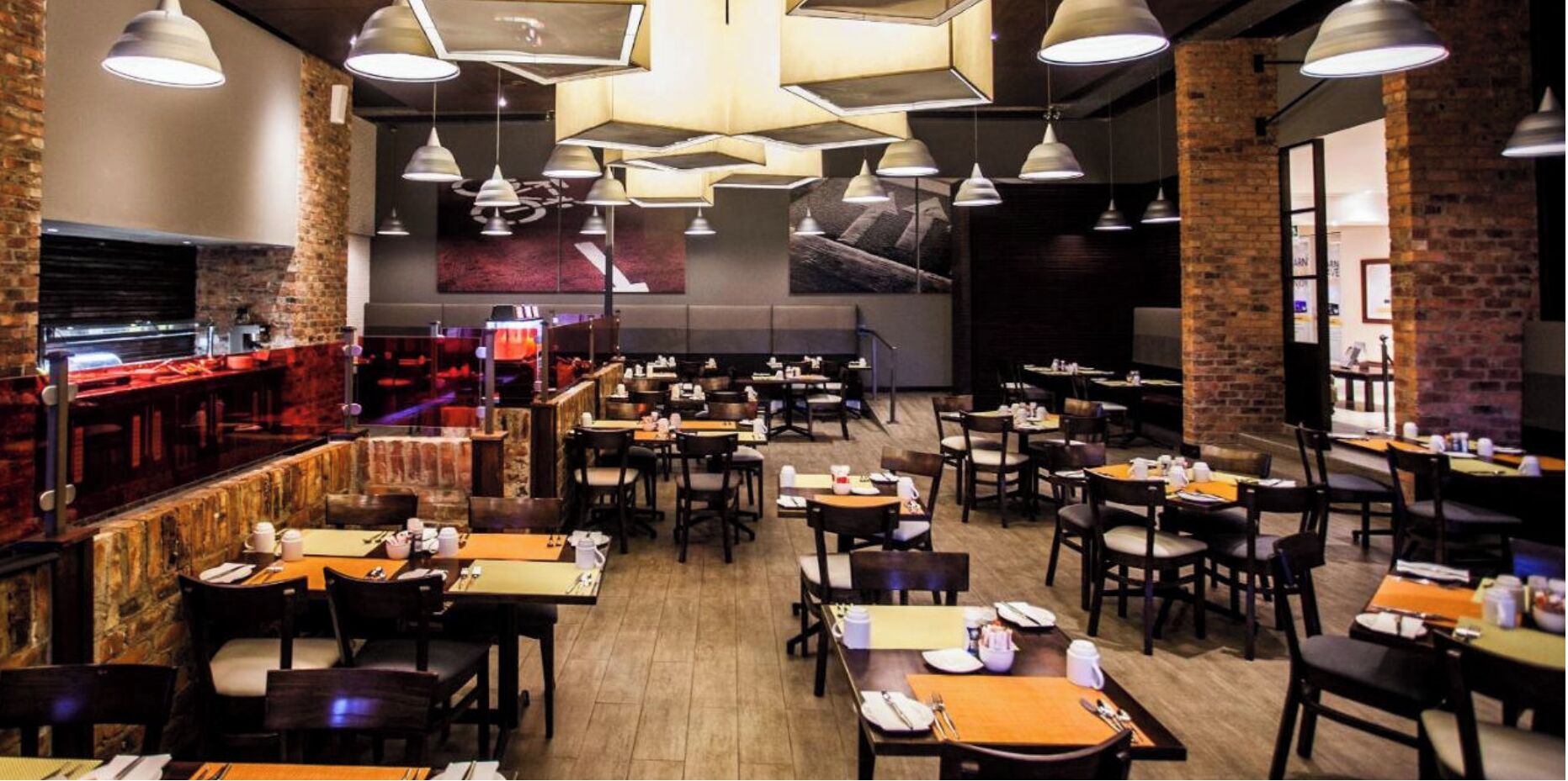A restaurant with multiple tables and chairs, a bar area, and hanging pendant lights.