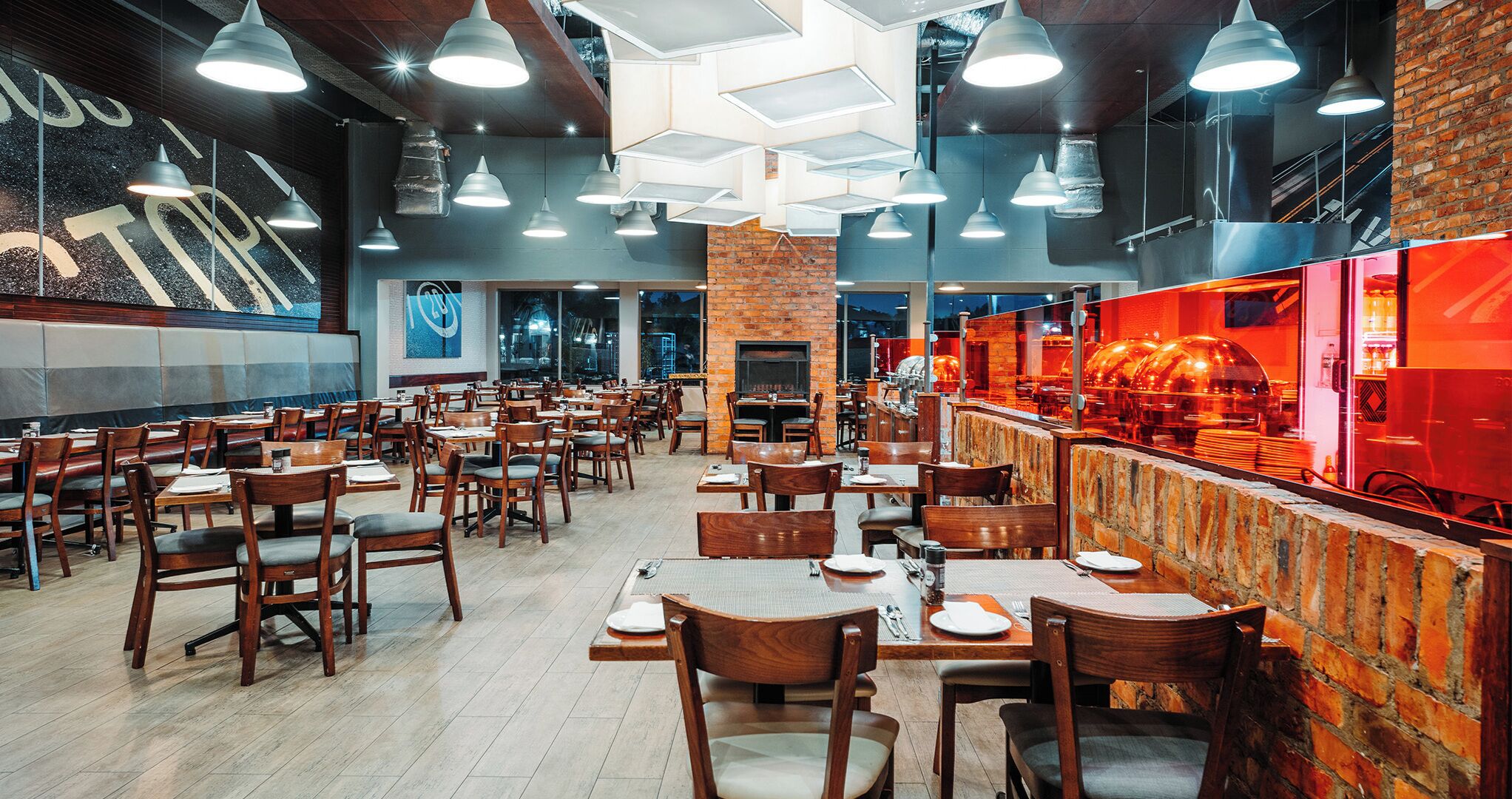 A restaurant with multiple tables and chairs, a brick wall, and hanging pendant lights.