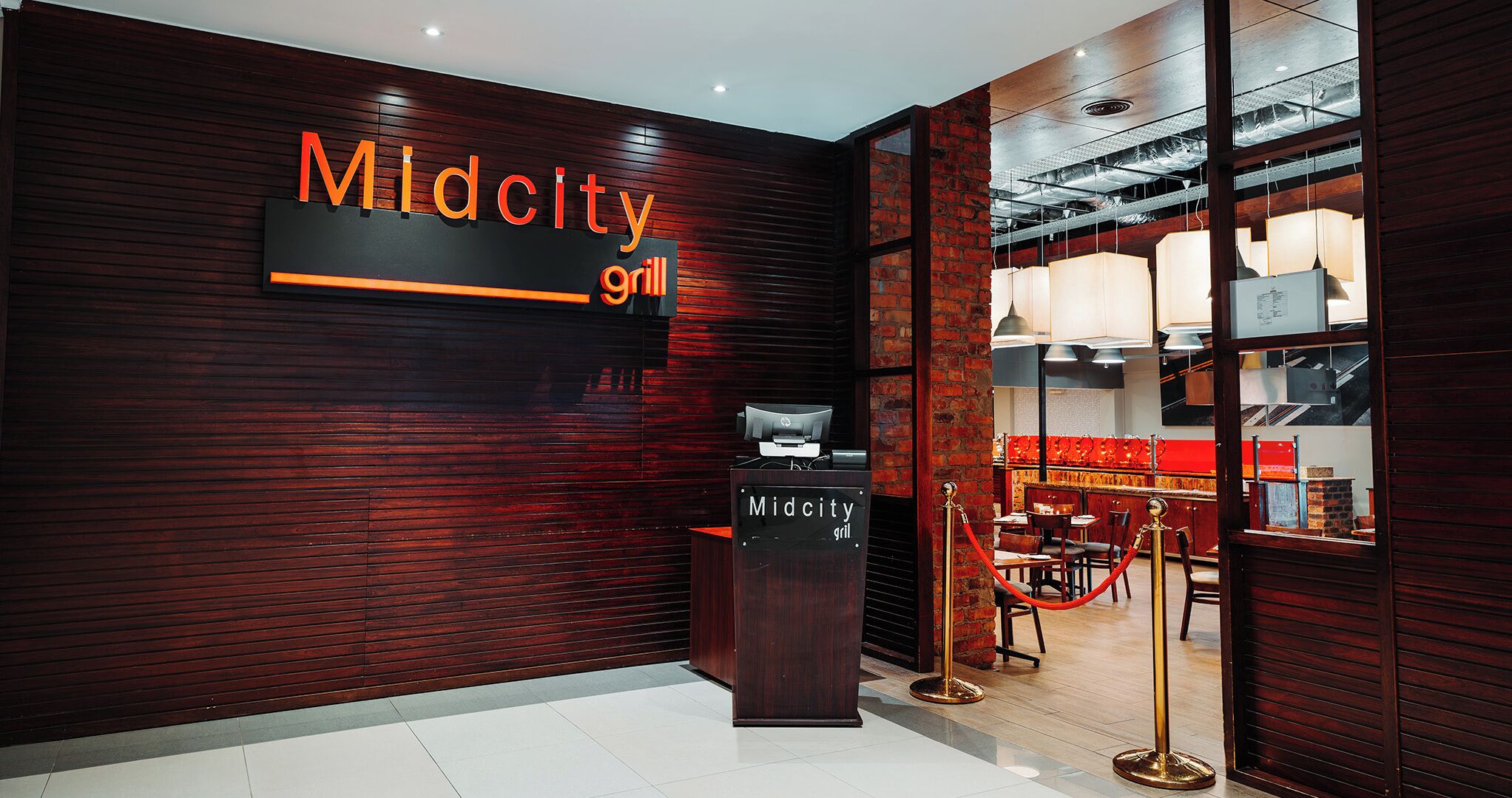 A restaurant interior with a dark wood panel wall, a sign reading "Midcity grill", and a counter with a menu display.
