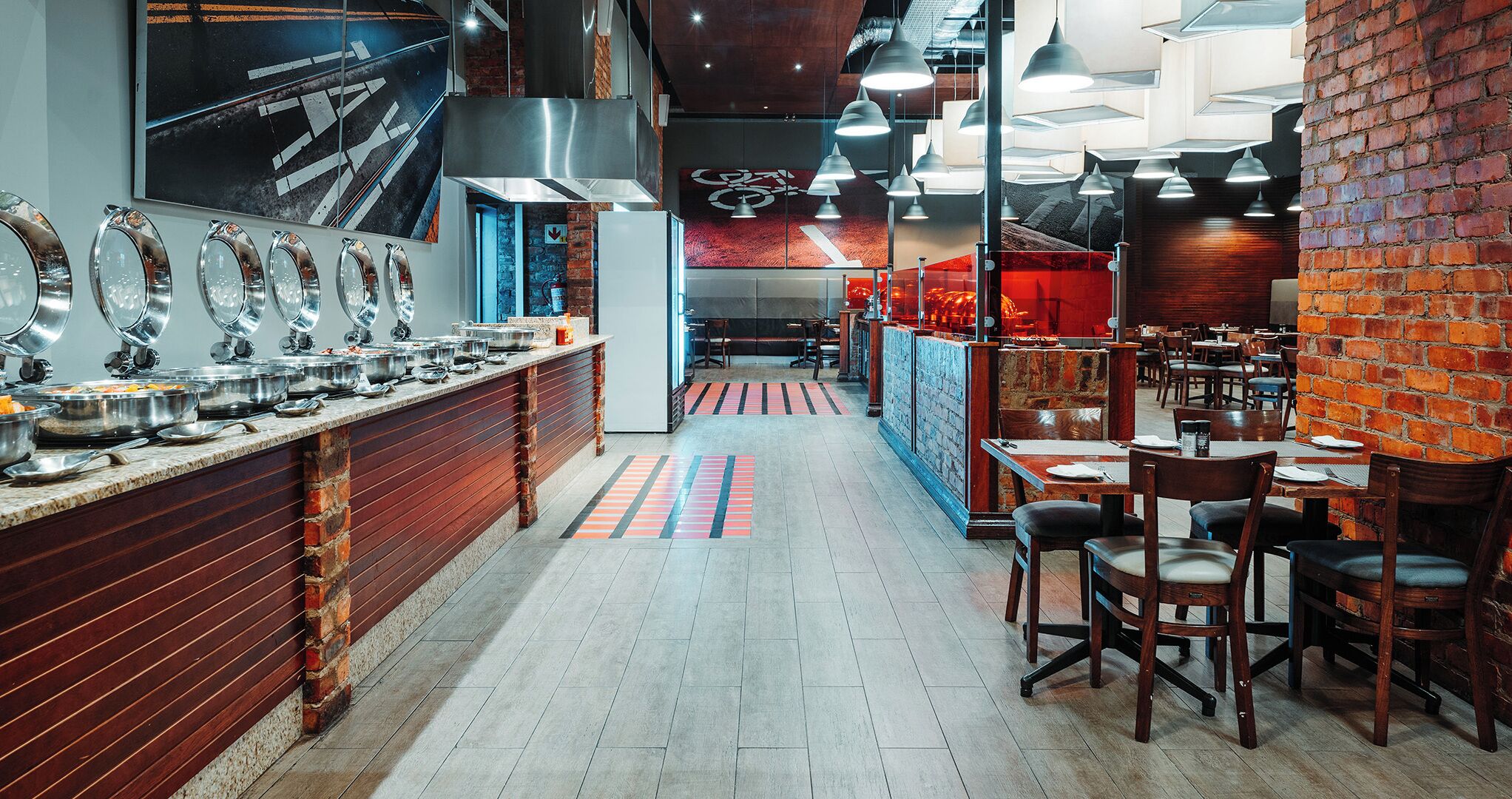 A restaurant with a long counter, multiple dining tables, and a brick wall.