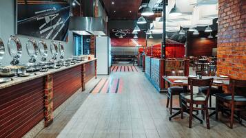 A restaurant with a long counter, multiple dining tables, and a brick wall.