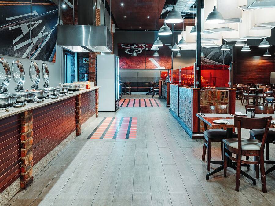 A restaurant with a long counter, multiple dining tables, and a brick wall.