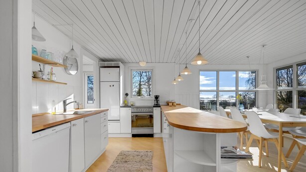 A modern kitchen with white cabinetry, a wooden countertop, and a built-in oven. There is a dining area with a wooden table and chairs, and large windows providing natural light. - 4 bedroom cozy home in Odder (Odder)