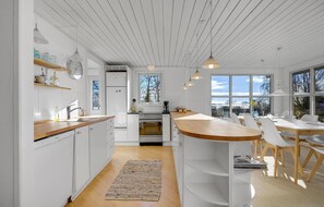 A modern kitchen with white cabinetry, a wooden countertop, and a built-in oven. There is a dining area with a wooden table and chairs, and large windows providing natural light. - 4 bedroom cozy home in Odder (Odder)