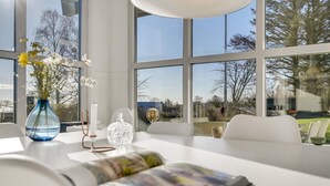 A modern interior with large windows, a table with a vase of flowers, a candle, and a magazine. - 4 bedroom cozy home in Odder (Odder)