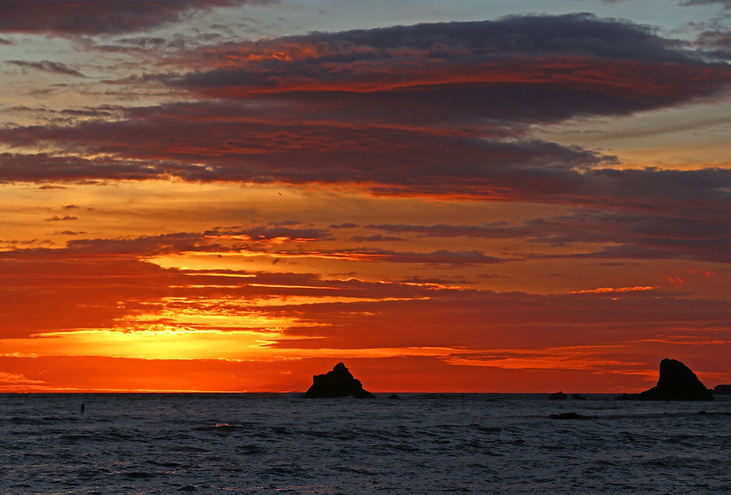 A sunset over the ocean with rock formations in the distance.