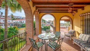 A balcony with a round table and chairs, a sofa, and a view of the surrounding neighborhood. - Noria Del Mar (Almuñecar)