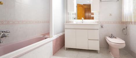 A bathroom with a bathtub, a sink, and a toilet. There is a mirror above the sink and a towel rack on the wall.
